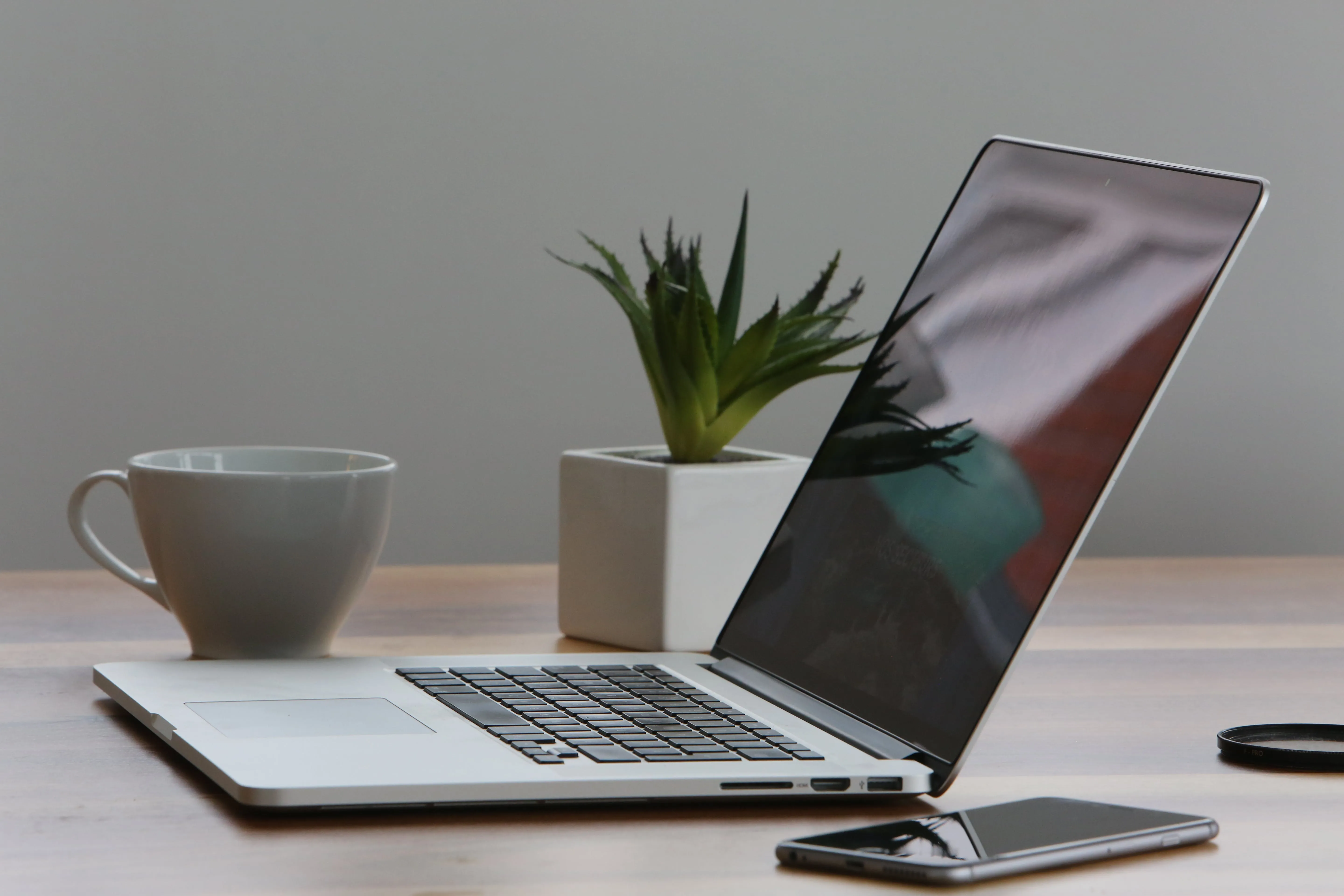 A laptop and cell phone on a desk next to a plant and coffee cup. Modern technology workspace